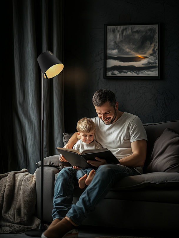 Ein gemütlicher Abend auf dem Sofa erleuchtet von Stehlampe. Ein Vater liest seinem Kind aus einem Buch vor.