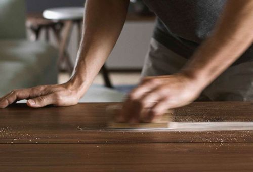 Eine Mann schleift einen Holztisch ab.